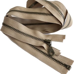 May include: A beige zipper with a brass finish. The zipper is closed and has a pull tab with the brand name "YKK" on it.