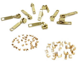 May include: A set of gold-colored zipper pulls and slider stops. The zipper pulls are in various styles, including a simple rectangular shape and a more ornate design with a decorative loop. The slider stops are small, metal pieces that are used to secure the zipper slider in place.