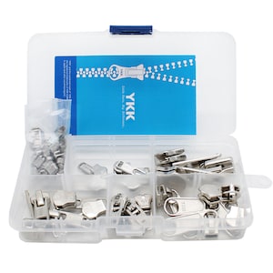 Puede incluir: Una caja de almacenamiento de plástico transparente llena de tiradores de cremallera plateados. La caja tiene una etiqueta azul con el texto "YKK Little Parts, Big Difference."