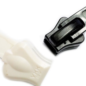 May include: Two zipper pulls, one black and one white, with the brand name "YKK" printed on each.