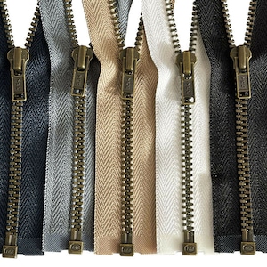 Pode incluir: Cinco fitas de zíper diferentes com puxadores de zíper de latão antigo. As fitas são pretas, cinzas, bege, brancas e pretas.