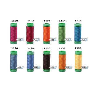 Könnte beinhalten: Eine Sammlung von zehn Spulen Aurifil 100% Baumwollgarn in verschiedenen Farben. Jede Spule ist zylindrisch mit einem grünen Deckel und Boden und einem Etikett mit einer Farbnummer. Die Farben umfassen Schattierungen von Rosa, Rot, Orange, Grün, Blau und Gelb.