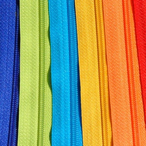 May include: A close-up of a variety of colorful zipper tapes. The tapes are arranged in a rainbow pattern, with the colors teal, blue, green, light blue, yellow, orange, red, and pink.