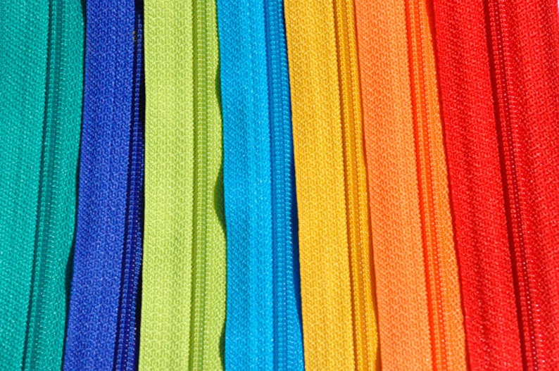 May include: A close-up of a variety of colorful zipper tapes. The tapes are arranged in a rainbow pattern, with the colors teal, blue, green, light blue, yellow, orange, red, and pink.