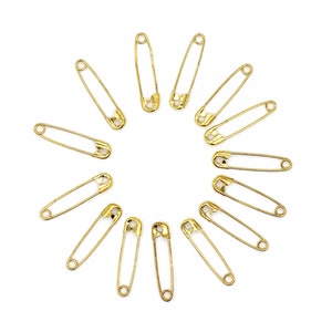 May include: A set of twelve gold safety pins arranged in a circle on a white background.