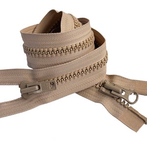 May include: A beige YKK two-way separating zipper with large plastic teeth and two matching sliders. The zipper tape is a light tan color, and the molded plastic teeth are a slightly darker beige. The sliders feature the YKK logo embossed.