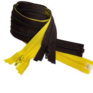 May include: A coiled roll of brown zipper tape with a yellow zipper. The zipper is open at the end, revealing the teeth and slider. The brown zipper is closed. The background is white.