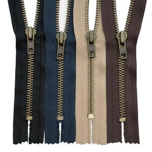 Puede incluir: Cuatro cremalleras de metal con cinta de tela en negro, azul marino, beige y marrón oscuro. Cada cremallera cuenta con un deslizador y tirador de metal en tono bronce, con dientes metálicos a juego a lo largo de las tiras de tela.