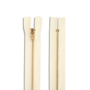 May include: A white zipper with a gold metal slider. The zipper is closed and has a herringbone pattern.