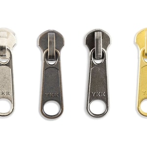 May include: Four zipper pulls in different finishes: silver, black, antique brass, and gold. Each pull has the YKK logo.