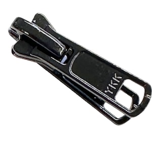 May include: Black metal zipper pull with a YKK logo. The pull has a rectangular shape with a rounded top and a small opening on the side.