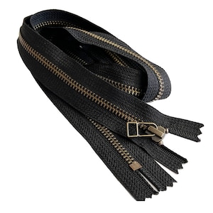 May include: A close-up of a black zipper with brass teeth. The zipper is folded in half and the ends are visible.