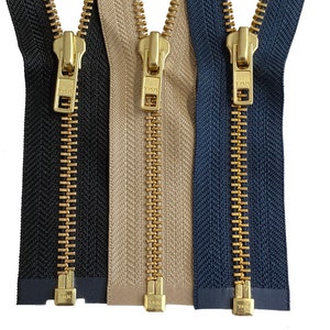 May include: Three metal zippers with gold teeth and pulls. The zippers are black, beige, and navy blue.