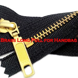 Pode incluir: Um z&iacute;per preto com um cursor e um puxador de metal dourado. O z&iacute;per &eacute; etiquetado "YKK #5 Brass Long Pull for Handbag Slider".