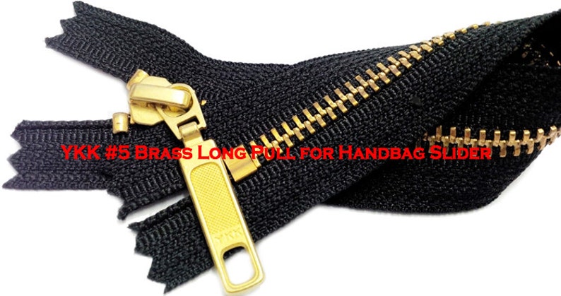 Pode incluir: Um z&iacute;per preto com um cursor e um puxador de metal dourado. O z&iacute;per &eacute; etiquetado "YKK #5 Brass Long Pull for Handbag Slider".