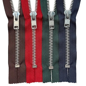 May include: Four metal zippers with fabric tape in brown, red, dark green, and navy blue. Each zipper features a silver-toned metal pull tab with the YKK logo embossed on the front, attached to a silver-toned metal chain and a rectangular bottom stop.