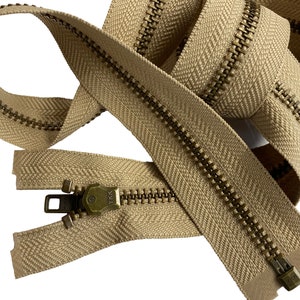 May include: A beige zipper with brass teeth and a YKK pull tab. The zipper is coiled and ready to be used for sewing projects.