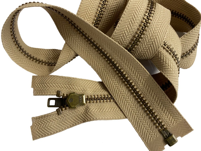 May include: A beige zipper with brass teeth and a YKK pull tab. The zipper is coiled and ready to be used for sewing projects.