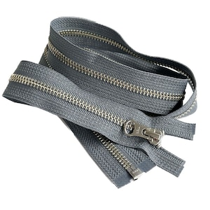 May include: A coiled, gray zipper with a silver-colored metal zipper pull and teeth. The zipper is made of a woven fabric and is designed for use in clothing or other sewing projects. The zipper is shown against a white background.