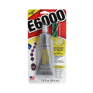 Könnte beinhalten: Eine durchsichtige Plastikflasche mit E6000 Schmuck- und Perlenkleber, einem dauerhaften Klebstoff, mit grüner Applikatorspitze. Die Flasche ist mit dem Produktnamen, der Größe und den Gebrauchsanweisungen versehen. Die Verpackung ist rot und gelb mit einem Bild einer Halskette.