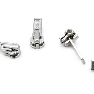 May include: Five silver zipper pulls, some with a slider and some with a pull tab. The zipper pulls are all metal and have a shiny finish.