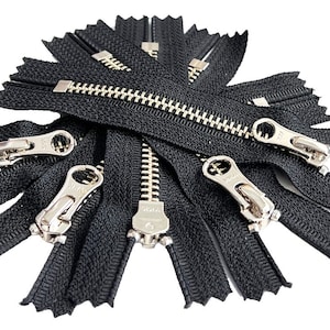 以下が含まれることがあります： 銀色の金属製の歯を持つ黒いジッパーのプルグループのクローズアップ。ジッパーはスターバーストパターンで配置されています。