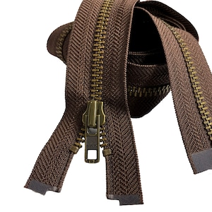 May include: Brown zipper tape with a brass zipper pull. The zipper tape is folded and the zipper pull is in the center of the image.
