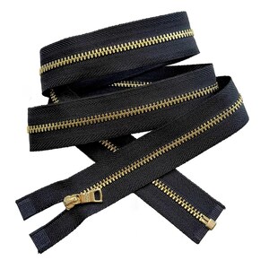 May include: A black zipper featuring metallic gold-toned teeth and a matching gold-toned metal slider. The zipper tape is made of a dark black fabric with a visible herringbone weave pattern, coiled in a layered arrangement against a white background.