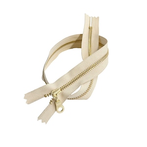 Könnte beinhalten: Ein beigefarbener Reißverschluss mit einem goldenen Metall-Schieber. Der Reißverschluss ist offen und die beiden Seiten sind getrennt.