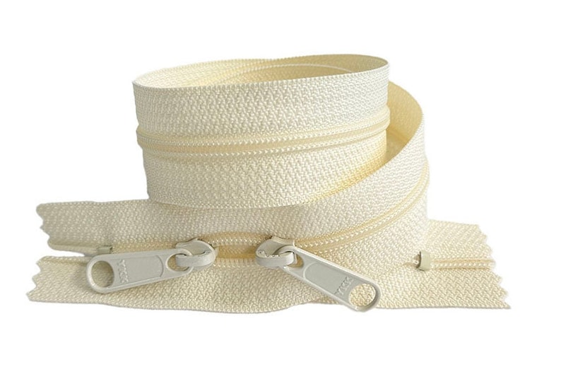 May include: A close-up of a white zipper tape with two silver zipper pulls. The zipper tape is coiled and the zipper pulls are visible at the bottom of the image.
