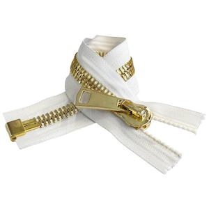 Op de afbeelding: Een witte rits met een gouden metalen schuif en tanden. De rits is dubbelgevouwen en de schuif bevindt zich in het midden van de afbeelding.