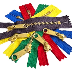 May include: Assortment of colorful zipper tapes with gold metal sliders. The zipper tapes are in red, green, blue, yellow, and purple.