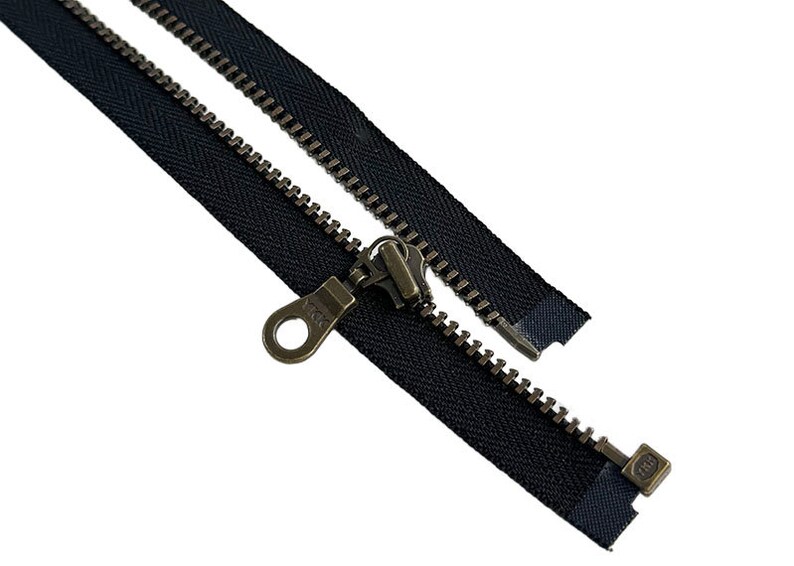 May include: A black zipper with antique brass hardware. The zipper is open and the slider is visible. The zipper is approximately 10 inches long.