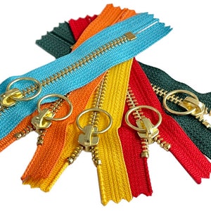 Può includere: Assortimento di tiretti per cerniere colorati con cursori e anelli in metallo dorato. Le cerniere sono di vari colori, tra cui blu, arancione, giallo, rosso e verde.