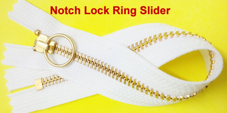 Pode incluir: Um z&iacute;per branco com um cursor de metal dourado e um puxador de anel. O z&iacute;per tem uma fun&ccedil;&atilde;o de trava de entalhe. O texto "Notch Lock Ring Slider" est&aacute; escrito em vermelho acima do z&iacute;per.