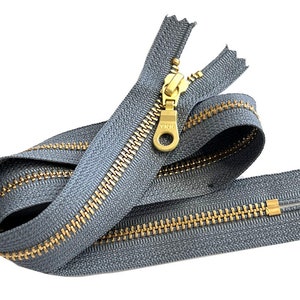 May include: A gray zipper with a brass slider and pull. The zipper is coiled and ready to be sewn into a garment.