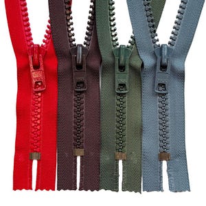 May include: Four YKK zippers in red, dark brown, olive green, and slate blue. Each zipper features a matching plastic pull tab, a continuous row of molded plastic teeth, and a small metal bottom stop at the base of the fabric tape.