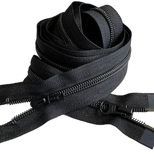 May include: Black zipper tape with black zipper pulls. The zipper tape is coiled and the zipper pulls are open.