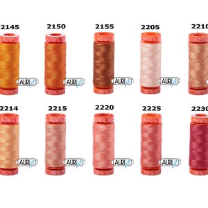 May include: Ten spools of Aurifil thread in various shades of orange, peach, and pink. The spools are labelled with the Aurifil logo and the thread number.