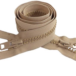 May include: A beige plastic zipper coiled into a circular shape, featuring two matching beige sliders at the ends. The zipper tape and teeth are a uniform light tan color, with a visible interlocking tooth design and two pull tabs attached.