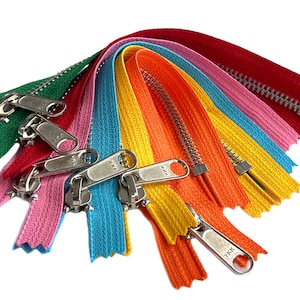 May include: Assortment of colorful zipper tapes with metal sliders. The tapes are in shades of green, pink, blue, yellow, orange, and red. The sliders are silver and have the text "YKK" on them.