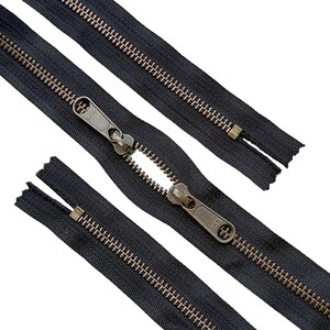 May include: Two black zips with antique brass-toned metal teeth and matching sliders. Each slider is clearly embossed with the YKK brand logo. The zips feature a durable fabric tape and are shown in a partially open position against a white background.