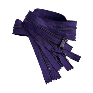 May include: A close-up of a bundle of purple zipper tape. The tape is folded and stacked, showing the zipper teeth and the slider.
