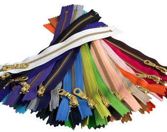 May include: A collection of colorful zippers in various shades, including white, black, blue, green, and red. Each zipper features a brass-colored metal pull and teeth, arranged against a white background. The zippers are of different lengths and are fanned out.