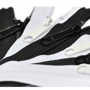 May include: A close-up of black and white zipper pulls. The zipper pulls are made of metal and have a smooth finish. The zipper pulls are arranged in a fan shape.