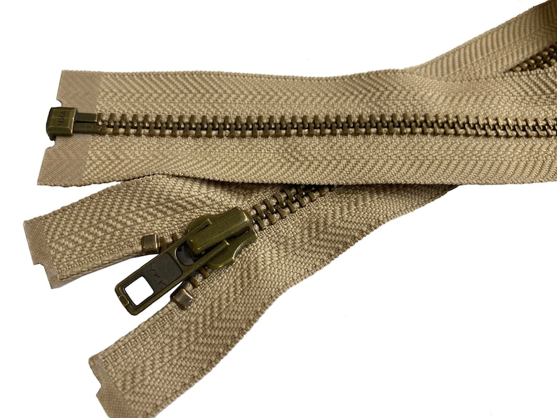 May include: A beige zipper with a brass slider and pull. The zipper is open and the teeth are visible.