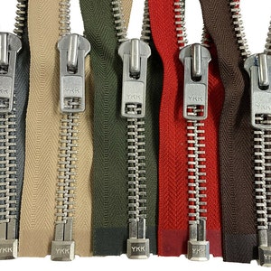 May include: Six metal zippers with different coloured tapes. The zippers are all YKK brand and have silver teeth. The tapes are grey, beige, green, red, brown, and black.