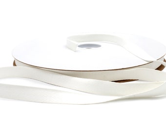 May include: A spool of white cotton twill tape. The tape is woven with a herringbone pattern and is wound around a cardboard core.