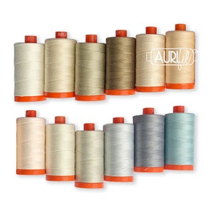 May include: A collection of 12 spools of Aurifil thread in various shades of beige, gray, and blue. The spools are arranged in two rows, with the top row featuring six spools and the bottom row featuring six spools.