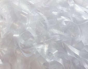 May include: A close-up of white, translucent, crinkled ribbon. The ribbon is piled in a heap, creating a textured, abstract background.